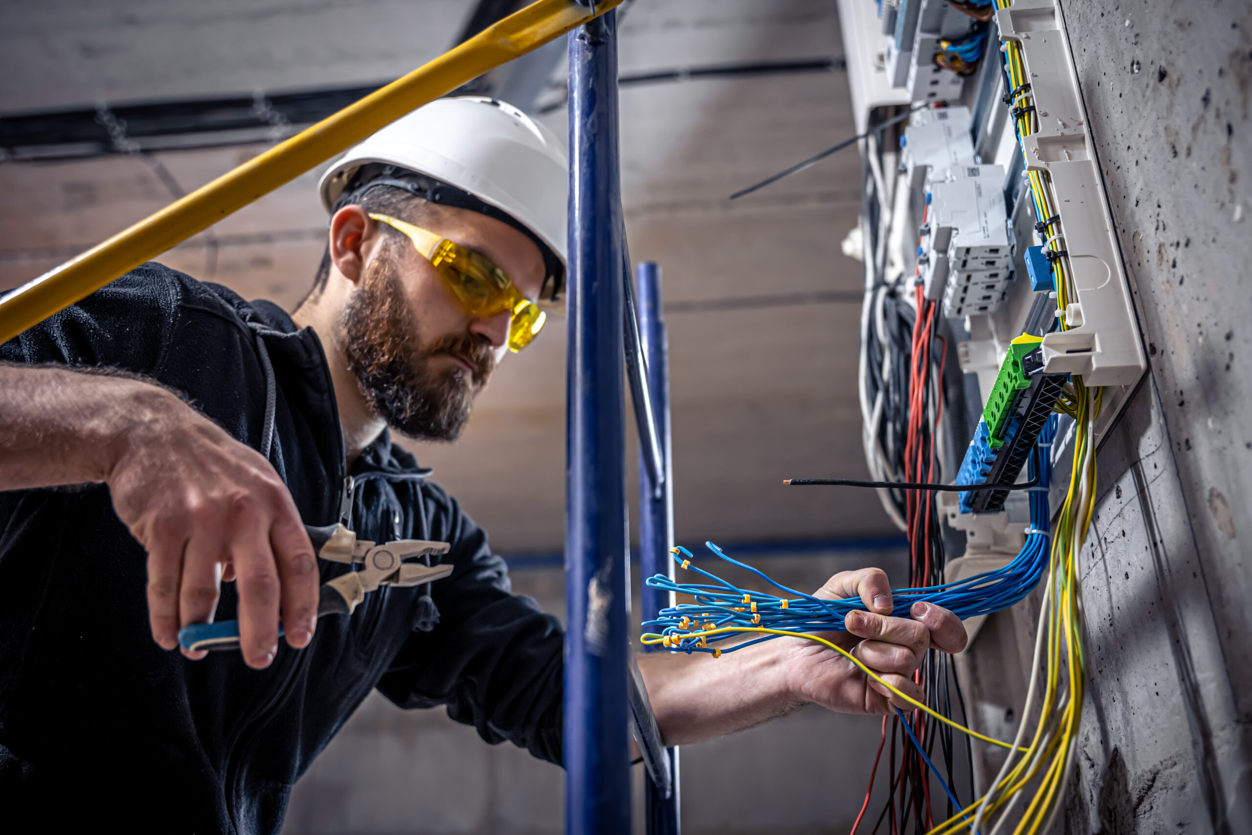 A male electrician works in a switchboard with an electrical connecting cable, connects the equipment with tools. deten insurance contractor